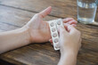 Woman hand holding blister pack of pills and glass of water on wooden table