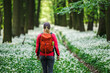 Female hiker with red backpack hiking in flowering forest. Hike in nature. Woman tourist walking in woodland