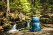Hiking backpack in forest by river near waterfall. Trekking equipment