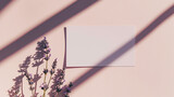 Fototapeta  - Cartão de papel branco em branco deitado nas sombras ao lado de algumas flores de lavanda em fundo rosa pálido. Vista superior, espaço de cópia