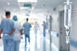 © AnastasiiaRozhmanova - blurred hospital corridor with the focus on an IV bag filled with clear liquid hanging prominently in the foreground. The blurred figures of doctors and nurses in the background un