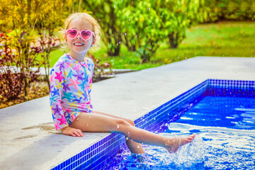 Wall Mural - Smiling cute little girl in sunglasses in pool in sunny day.