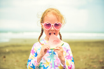 Wall Mural - Portrait of girl of 4 years with heart-shaped sunglasses on beach of Costa Rica eating watermelon