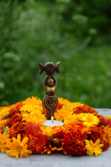 Poster - Triple Goddess figurine with candle and colorful flowers in garden, nature background. Symbol of the Triune Moon. esoteric ritual for Litha, Midsummer. witchcraft, wiccan spiritual practice.