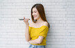 Excited beautiful Asian woman wearing yellow off-the-shoulders holding in hand smart phone talking with digital assistant or friend distantly uses easy voice messaging. Concept of modern ai technology