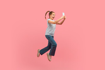 a young girl is captured mid-air, jumping energetically with a cell phone in hand. she appears joyfu