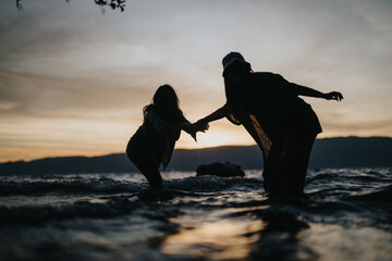 Wall Mural - Two girls sharing a joyous moment by the lake at sunset, symbolizing friendship and the happiness of free time in nature.