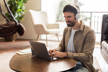 Aufkleber - A man is seated at a table, focused on his laptop screen, wearing headphones. He appears to be working or studying intently in a quiet environment.