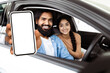 © Prostock-studio - A bearded Indian man is extending his arm out of a car window, holding a smartphone with a blank screen towards the camera possibly for an interactive display or advertising purpose.