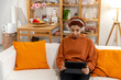 Beautiful african american girl with afro hairstyle wearing headphones smiling listening music at home indoor. Young woman enjoy listening favorite music on tablet. People lifestyle joy concept