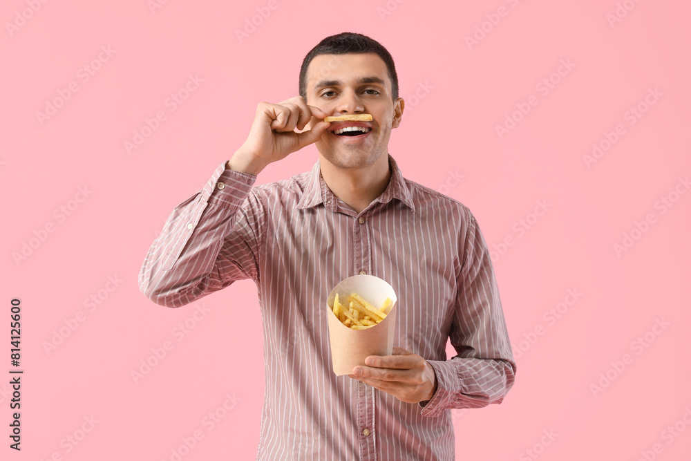 Young man with french fries on pink background