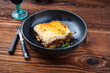 Traditional Greek moussaka with beef mince, eggplant and bechamel sauce served as close-up in a Nordic design Bowl on an old wooden board