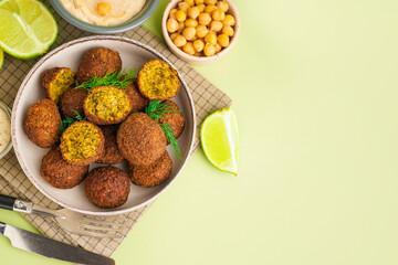 Wall Mural - Bowl with delicious falafel balls, hummus and lime on green background