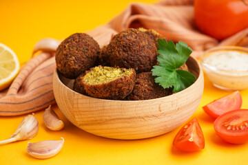 Wall Mural - Wooden bowl with delicious falafel balls, tomatoes and garlic on orange background, closeup