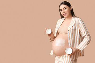 Wall Mural - Young pregnant woman with jars of body cream against color background