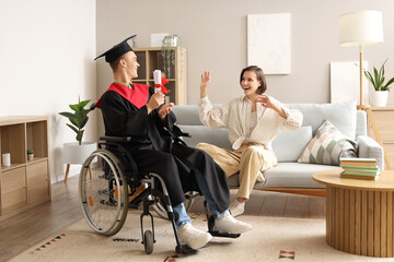 Wall Mural - Male graduate in wheelchair with diploma and his friend at home