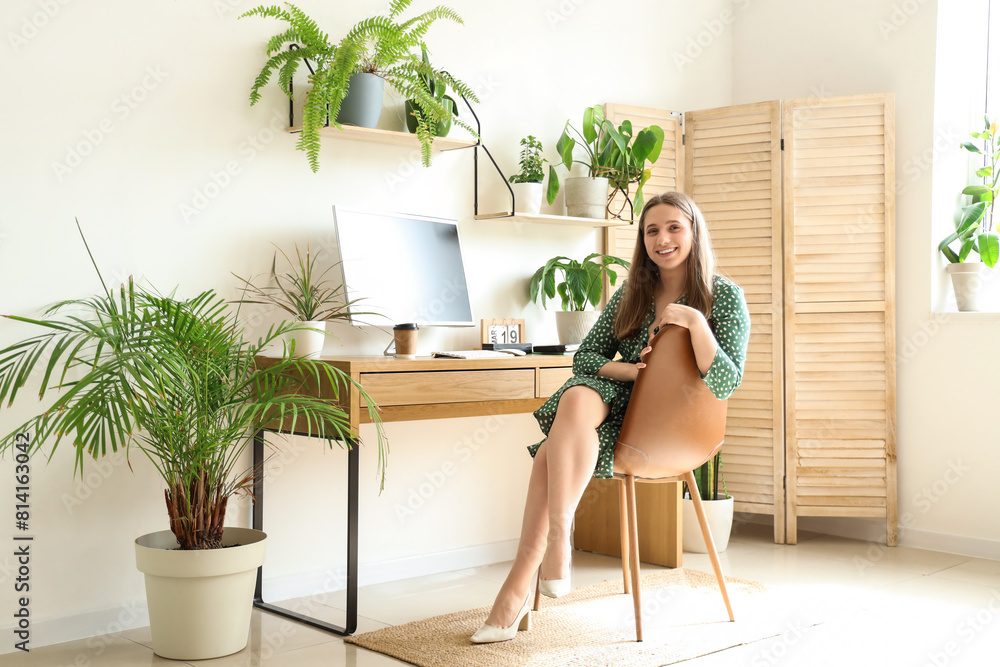 Young woman sitting at table with houseplants in office