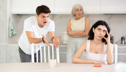 Poster - Domestic quarrel - offended young woman sits at the table while mother and young husband yell at her