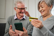 Senior couple man woman shopping online with smartphone paying with credit card. Old people buying on Internet enter credit card details at home indoors. Online shopping delivery service ecommerce