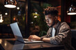 © fahrwasser - A black student using laptop and taking notes during an online class at a cozy coffee shop table during nighttime
