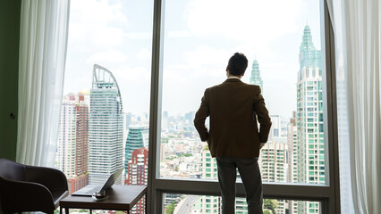 Wall Mural - Back view ambitious businessman standing in ornamented office gazing out window to cityscape skyline. Determination and business ambition drive business career toward to bright future