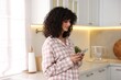 © New Africa - Beautiful young woman in stylish pyjama with smartphone in kitchen