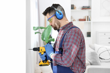 Wall Mural - Young worker in uniform using electric drill indoors