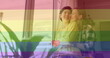 Image of heart emojis and rainbow flag over caucasian female couple embracing