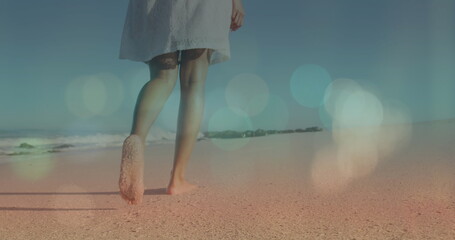 Wall Mural - Image of lens flare over low section of biracial young woman walking barefoot on sandy beach