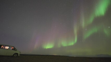 Wall Mural - Mesmerizing show of northern lights in the dark night sky above the sea. A small van stands under the lights.  A timelapse video.