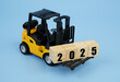 Yellow forklift truck carrying wooden cubes with numbers 2025 on blue background	