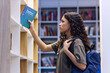 © Seventyfour - Side view portrait of young teen girl reaching for book on shelf in library