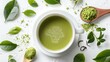 A cup of green tea surrounded by fresh green tea leaves and a spoonful of matcha powder on a white background