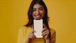 © VISUAL BACKGROUND - A woman holding up her phone on a yellow background.