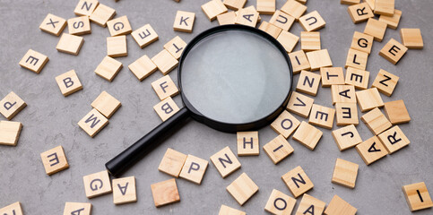 Wall Mural - Magnifying glass with many wood letters of English alphabets, learning English concept