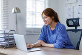 Fototapeta Sypialnia - Young asian business woman working at home office with laptop and papers on desk