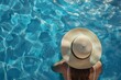 © Sabina Gahramanova - Top view of a woman wearing a sun hat relaxing at a swimming pool with blue water during a summer vacation, depicting a travel and spa concept.