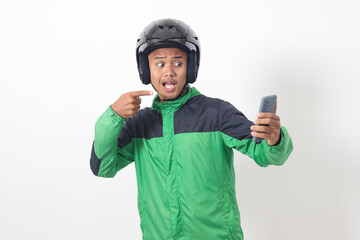 Wall Mural - Portrait of Asian online taxi driver wearing green jacket and helmet holding mobile phone while pointing to the side. Isolated image on white background