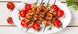 Top view of a plate containing grilled chicken skewers and cherry tomatoes on a white wooden table accompanied by a red napkin Ample copy space image available