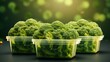 Three packages of fresh green broccoli florets in plastic containers on a dark surface with a blurred background.