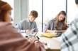 © Serhii - students sit at shared desk making notes studying together at university