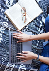 Above, laptop and typing with textbook for student in college or university in studying for exam or test. Top view, computer and hands for writing, assignment or essay in school, deadline or due date