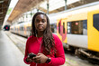 © ADDICTIVE STOCK - Black woman waiting at train station using smartphone