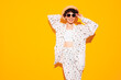 Young beautiful smiling female in trendy summer costume clothes. Carefree woman posing near yellow wall in studio. Positive model having fun indoors. Cheerful and happy. In hat and sunglasses
