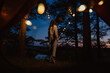 View from the tent. A young woman stands tall and holds lights in her hands against the background of trees and water. Outdoor recreation. The magic is in the picture.