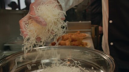 Wall Mural - Closeup footage of chef's hands putting rice noodles and fried fish sticks in big stainless bowl