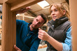 © Monkey Business - Carpenter With Female Apprentice In Workshop Using Ruler To Measure Wood Of Window Frame