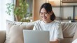 © 2April - Smiling woman using a laptop on a couch at home, suitable for content about remote work, online learning, or leisure activities.