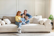 © Home-stock - Cheerful family of three sitting on couch in light living room, parent and their daughter enjoy time together at home. Parenthood happiness