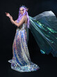 Full length portrait of beautiful female model with long purple hair wearing elf ears, a fantasy fairy crown and  rainbow glitter sequin ball gown. graceful standing pose,  isolated in dark studio bac